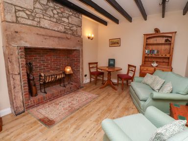 A sitting room with a stone fireplace wooden furniture and green upholstered seating at Rose Cottage Akeld near Wooler