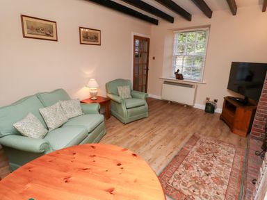 A living room with green sofa and armchair wooden table lamp and television at Rose Cottage Akeld near Wooler