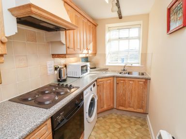 A kitchen with wooden cabinets a washing machine microwave toaster and a window at Rose Cottage Akeld near Wooler