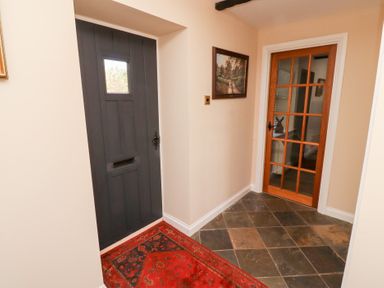 An entryway with a dark wooden door a red patterned rug a glass-paneled wooden interior door and a framed painting on the wall at Rose Cottage Akeld near Wooler
