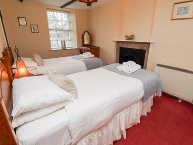 A bedroom with two single beds a window a dresser and a fireplace at Rose Cottage in Akeld near Wooler