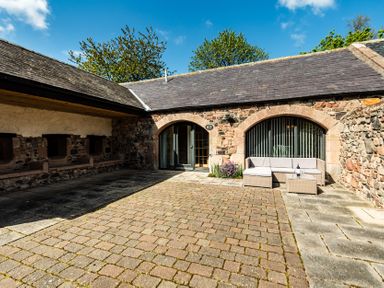 An outdoor seating area with stone walls and paved surface at Lupin Cottage near Wooler