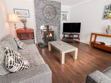 A living room with a sofa a coffee table a TV on a stand a stone fireplace with a clock and a wooden cabinet with books at 17 Clover Hill in Killorglin County Kerry