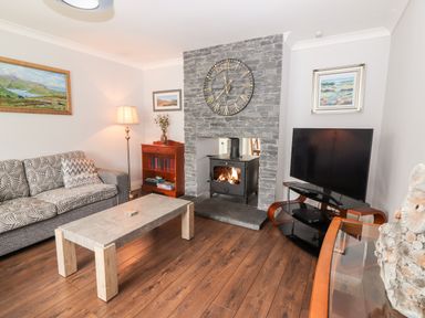 A living room with a stone fireplace and clock a television on a stand a sofa and a coffee table at 17 Clover Hill in Killorglin County Kerry