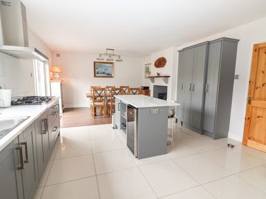 A kitchen with grey cabinets an island wooden dining table with chairs and a painting on the wall at 17 Clover Hill in Killorglin County Kerry