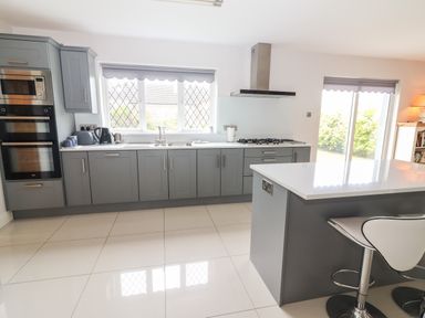 A kitchen with gray cabinets a white countertop built in oven microwave and stove with a window and sliding door at 17 Clover Hill in Killorglin County Kerry