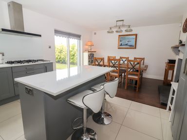 A kitchen with a gray island and two white bar stools adjoining a dining area with wooden table and chairs at 17 Clover Hill in Killorglin County Kerry