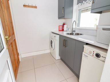 A laundry room with washing machine dishwasher sink window and wooden door at 17 Clover Hill in Killorglin County Kerry