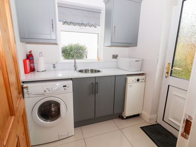 A laundry room with a washing machine a sink cabinets and a door at 17 Clover Hill in Killorglin County Kerry
