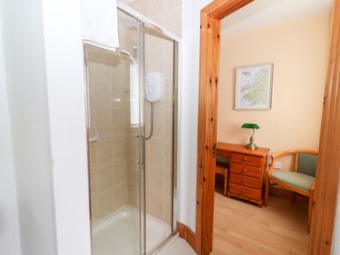 A bathroom with a tiled shower enclosure and a room with a wooden desk a green lamp a framed map on the wall and a wooden chair at 17 Clover Hill in Killorglin County Kerry