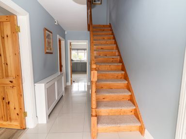 A hallway with wooden stairs carpet on steps radiator cover on left wall at 17 Clover Hill in Killorglin County Kerry