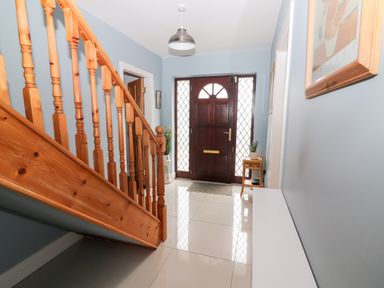 A hallway with a wooden staircase a dark wooden front door and light blue walls at 17 Clover Hill in Killorglin County Kerry