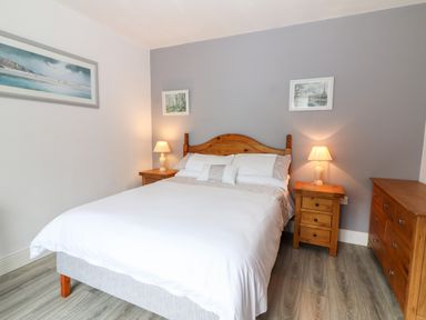 A bedroom with a bed with white bedding two bedside tables with lamps a wooden dresser and three framed pictures on the walls at 17 Clover Hill in Killorglin County Kerry