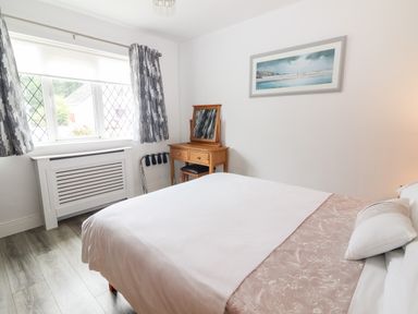 A bedroom with a bed a wooden dressing table and a window with patterned curtains at 17 Clover Hill in Killorglin County Kerry