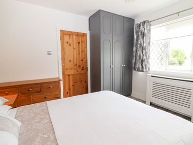 A bedroom with a wooden door gray wardrobe window with patterned curtains and a wooden dresser at 17 Clover Hill in Killorglin County Kerry