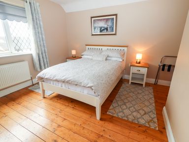 A bedroom with a bed two bedside tables with lamps a window and wooden floor at 17 Clover Hill in Killorglin County Kerry