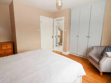 A bedroom with a bed a white wardrobe a wooden chest of drawers a grey armchair and an open door to a bathroom at 17 Clover Hill in Killorglin County Kerry