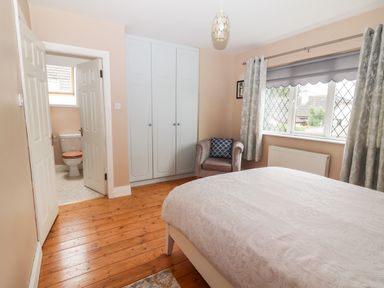 A bedroom with a bed a window with curtains a wardrobe an armchair and an open door leading to a bathroom at 17 Clover Hill in Killorglin County Kerry