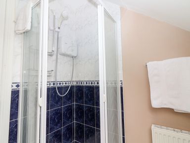 A shower cubicle with white and dark blue tiled walls and a white towel hanging on a rail at 17 Clover Hill in Killorglin County Kerry