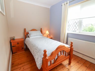 A bedroom with a single wooden bed beside two wooden nightstands one with a lamp and the other with small decor items at 17 Clover Hill in Killorglin County Kerry