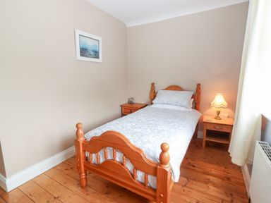 A bedroom with a single wooden bed a bedside table with a lamp and a painting on the wall at 17 Clover Hill in Killorglin County Kerry