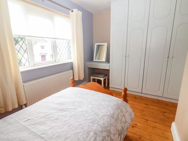 A bedroom with a bed a dressing table a stool large white wardrobes and a window with curtains at 17 Clover Hill in Killorglin County Kerry
