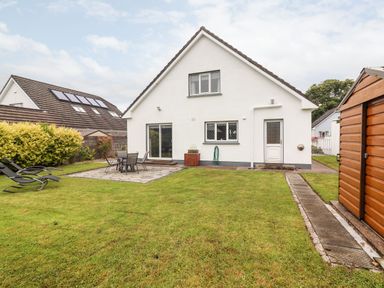 A backyard with a white house a patio table and chairs lawn chairs a wooden shed and grass at 17 Clover Hill in Killorglin County Kerry