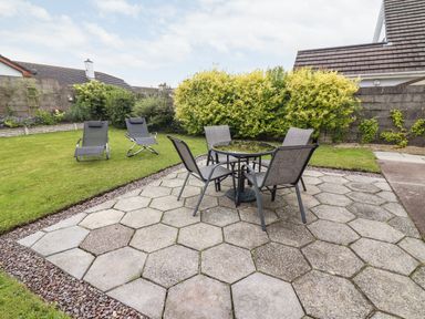 A backyard with a hexagonal patio table and four chairs and two lounge chairs on grass at 17 Clover Hill in Killorglin County Kerry