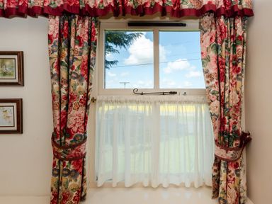 A window with floral curtains and framed pictures at Bramble Cottage Akeld near Wooler
