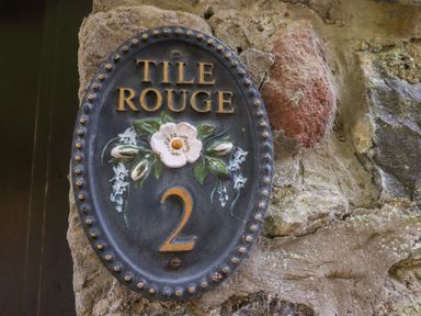 A decorative house number plaque with the text Tile Rouge 2 on a stone wall at Tile Rouge in Wooler