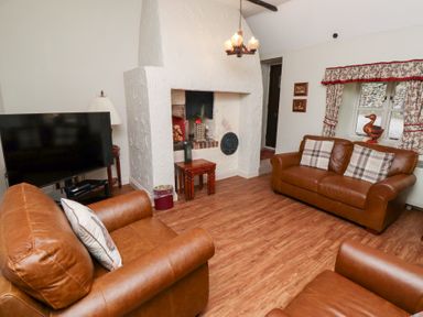 A living room with brown leather sofas a television and a fireplace at Tile Rouge in Wooler