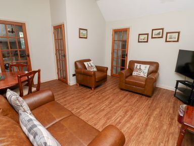 A living room with leather armchairs sofa wooden dining table and television at Tile Rouge in Wooler