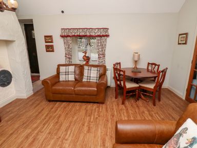A living room with leather sofas a wooden dining table with chairs and patterned curtains at Tile Rouge in Wooler