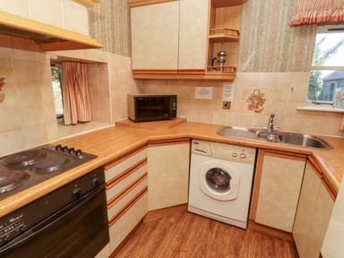 A kitchen with an electric stove oven microwave washing machine and stainless steel sink at Tile Rouge in Wooler