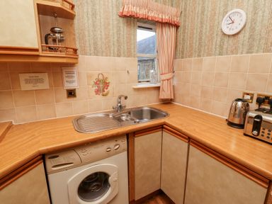 A kitchen corner with a washing machine under the counter a double sink a kettle and toaster on the countertop a window with curtains and a wall clock at Tile Rouge in Wooler