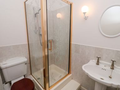 A bathroom with a shower enclosure a toilet with a wooden seat and a white sink with two taps and a round mirror at Tile Rouge in Wooler