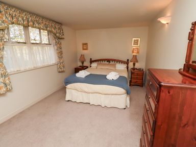 A bedroom with a double bed bedside tables lamps a wooden dresser and floral curtains at Tile Rouge in Wooler