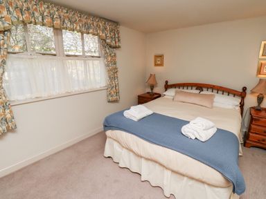 A bedroom with a double bed two bedside tables lamps and a window with floral curtains at Tile Rouge in Wooler