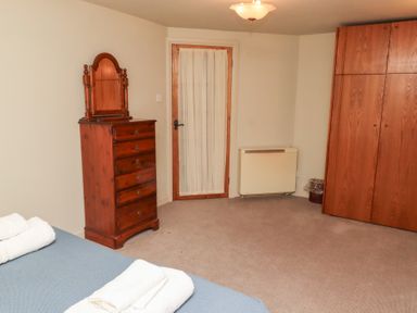 A bedroom with a wooden dresser with a mirror wooden wardrobes a door with a curtain and a bed with towels at Tile Rouge in Wooler