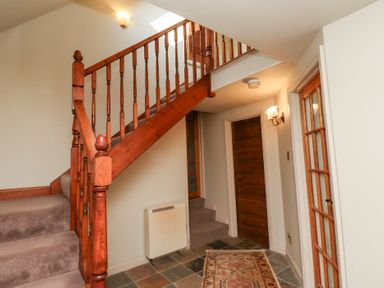 A hallway with wooden stairs carpeted steps a patterned rug tiled floor a wooden door and a wall-mounted light at Tile Rouge in Wooler