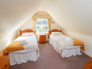 A bedroom with two single beds a window a wooden nightstand and floral curtains at Tile Rouge in Wooler