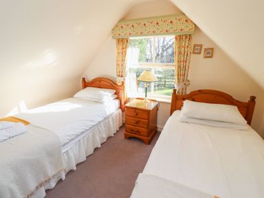 A bedroom with two single beds a bedside table and a window with floral curtains at Tile Rouge in Wooler