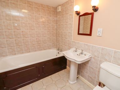 A bathroom with a bathtub sink toilet mirror and wall lights at Tile Rouge in Wooler