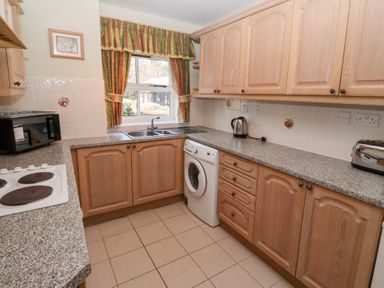 A kitchen with wooden cabinets a washing machine a microwave kettle and toaster at Pansy Plot in Akeld near Wooler