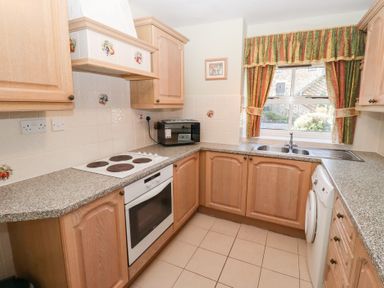 A kitchen with wooden cabinets a stove oven microwave and a window with curtains at Pansy Plot in Akeld near Wooler
