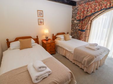 A bedroom with two single beds wooden nightstand with lamp and stone wall with floral curtains at Pansy Plot in Akeld near Wooler