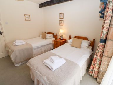 A bedroom with two single beds a nightstand with a lamp and floral curtains at Pansy Plot in Akeld near Wooler