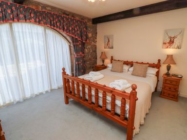A bedroom with a wooden bed and two bedside tables with lamps and animal paintings at Pansy Plot in Akeld near Wooler