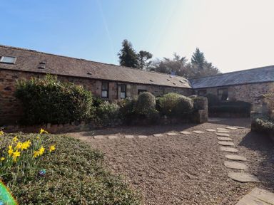 A stone cottage with a gravel courtyard and shrubs at Pansy Plot in Akeld near Wooler