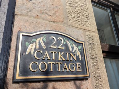 A house number plaque 22 Catkin Cottage mounted on a stone wall beside a window at Catkin Cottage Akeld near Wooler